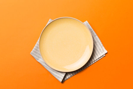 Top view on colored background empty round yellow plate on tablecloth for food. Empty dish on napkin...