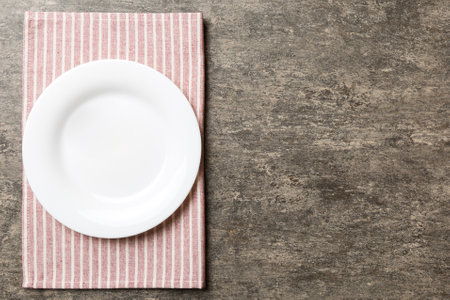 Top view on colored background empty round white plate on tablecloth for food. Empty dish on napkin with space for your design.の写真素材