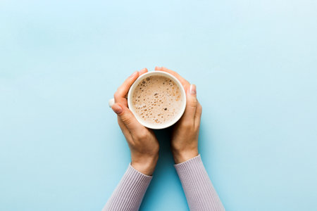 Minimalistic style woman hand holding a cup of coffee on Colored background. Flat lay, top view...