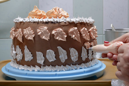 A woman pastry chef with a pastry bag in her hands squeezes cream on a cake in a home kitchen....