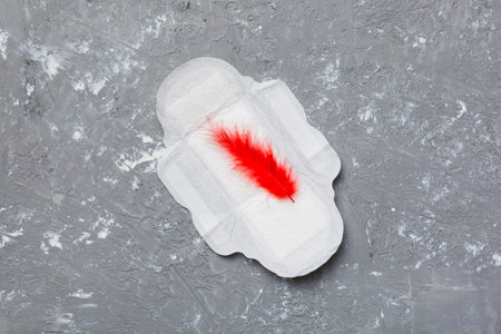 Women hygiene products or Sanitary pad with red feather on colored background. pastel color. closeup. Empty place for text. Female daily hygiene.の写真素材