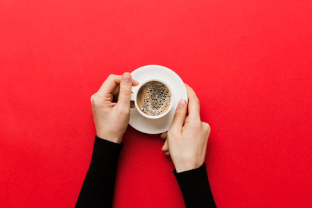 Minimalistic style woman hand holding a cup of coffee on Colored background. Flat lay, top view cappuccino cup. Empty place for text, copy space. coffee addiction. Top view, flat lay.の写真素材