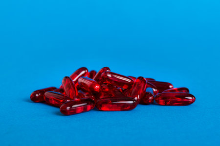 Heap of red pills on colored background. Tablets scattered on a table. Pile of red soft gelatin capsule. Vitamins and dietary supplements concept.の写真素材