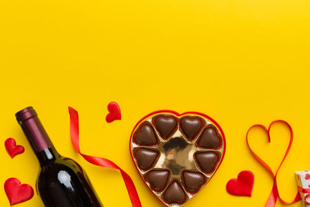 Bottle of red wine on colored background for Valentine Day with gift and chocolate. Heart shaped with gift box of chocolates top view with copy space.の写真素材