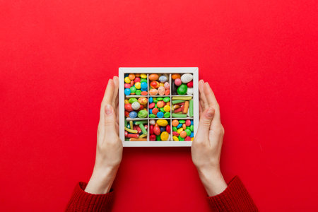 Female hands with delicious candies in box on color background.
