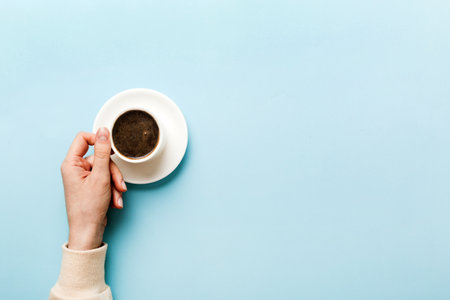 Minimalistic style woman hand holding a cup of coffee on Colored background. Flat lay, top view espresso cup. Empty place for text, copy space. coffee addiction. Top view, flat lay.の写真素材