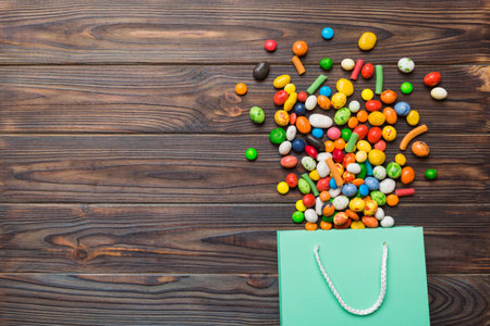 shopping paper gift bag in corner full of assorted traditional candies falling out on colored...