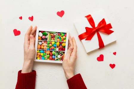 Female hands with delicious candies in box on color background.の写真素材