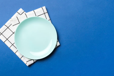 Top view on colored background empty round Blue plate on tablecloth for food. Empty dish on napkin...