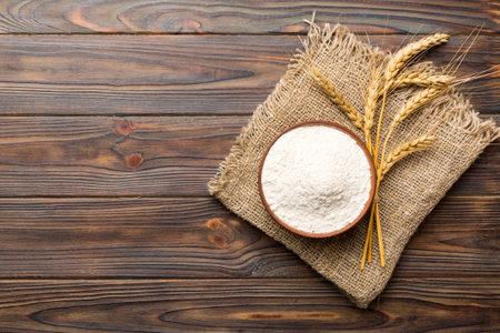 Flat lay of Wheat flour in wooden bowl with wheat spikelets on colored background. world wheat...