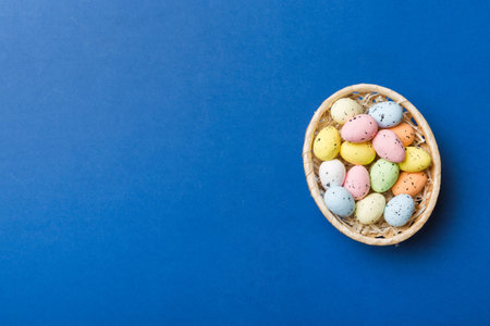 Colorful Easter eggs in wicker basket against colored background, closeup. top view with copyspace.