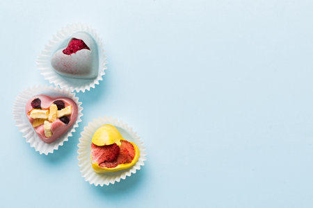 chocolate sweets in the form of a heart with fruits and nuts on a colored background. top view with...