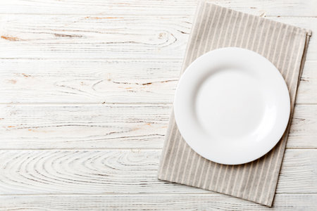 Top view on colored background empty round white plate on tablecloth for food. Empty dish on napkin...