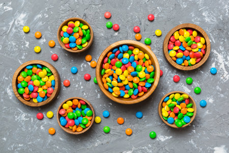 different colored round candy in bowl and jars. Top view of large variety of sweets and candies with...