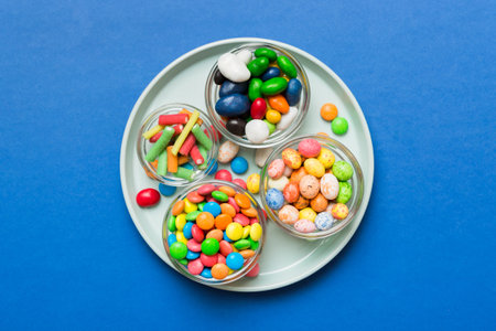 Multicolored candies in a bowl on a colored background. birthday and holiday concept. Top view with copy space.の写真素材