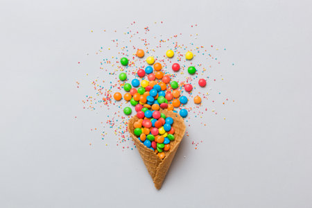 waffle cone full of assorted traditional candies falling out on colored background with copy space....