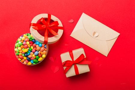 Red envelope with candy and gift box and Valentines hearts on colored background. Flat lay, top view. Romantic love letter for Holiday concept.の写真素材