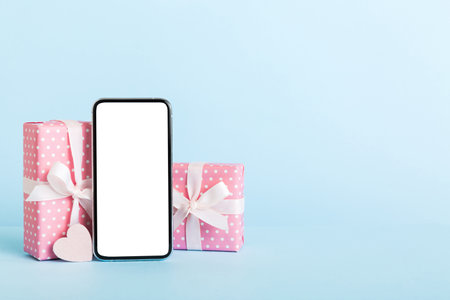 mobile phone with blank screen on colored background with hearts, calendar and gift box, valentine day concept perspertive view flat lay.の写真素材