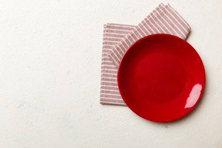Top view on colored background empty round red plate on tablecloth for food. Empty dish on napkin with space for your design.の写真素材