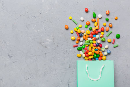 shopping paper gift bag in corner full of assorted traditional candies falling out on colored background with copy space. Happy Holidays sale concept.の写真素材