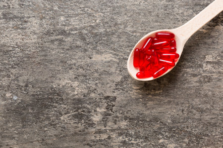 Vitamin capsules in a spoon on a colored background. Pills served as a healthy meal. Red soft gel vitamin supplement capsules on spoon.の写真素材