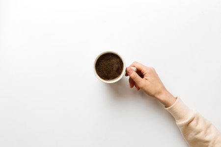 Minimalistic style woman hand holding a cup of coffee on Colored background. Flat lay, top view cappuccino cup. Empty place for text, copy space. coffee addiction. Top view, flat lay.の写真素材