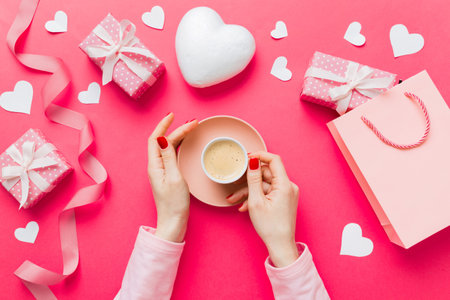 Flat lay of heart shaped cup of black coffee in the hands of women on colored background with copy space top view. Valentine day and holiday concept.の写真素材
