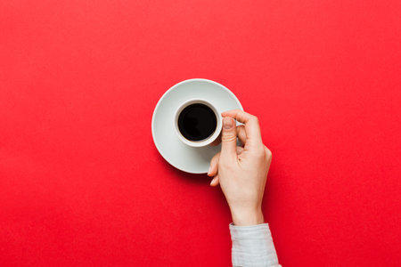 Minimalistic style woman hand holding a cup of coffee on Colored background. Flat lay, top view espresso cup. Empty place for text, copy space. coffee addiction. Top view, flat lay.の写真素材