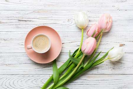 Spring background with flowers, a cup of coffee and a bouquet of pink and white tulips on colored table background with place for text. Copy space top view.の写真素材