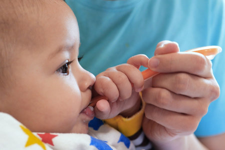 Portrait of little baby boy eating food. Baby with a spoon in feeding chair. Cute baby eating first meal.の写真素材