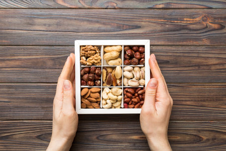 Young woman holding box with different nuts, closeup. Close up, copy space, top view, flat lay. Walnut, pistachios, almonds, hazelnuts and cashews.の写真素材