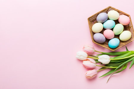 Happy Easter composition. Easter eggs in basket on colored table with yellow Tulips. Natural dyed colorful eggs background top view with copy space.の写真素材