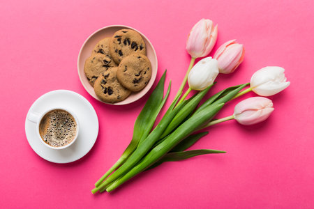 Cup of coffee mug with coffee, cookies and tulips on a colored background. Greeting spring card top view.の写真素材