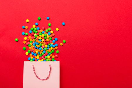 shopping paper gift bag in corner full of assorted traditional candies falling out on colored background with copy space. Happy Holidays sale concept.の写真素材