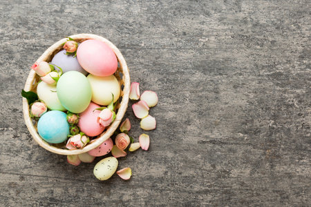 Happy Easter. Easter eggs in basket on colored table with yellow roses. Natural dyed colorful eggs background top view with copy space.の写真素材
