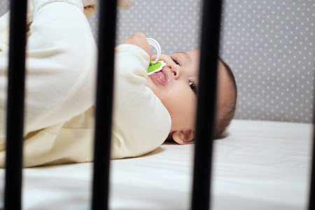 Baby sucking Pacifier looking on bed. portrait of cute newborn baby lying on bed with pacifier on mouth.の写真素材