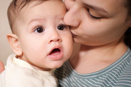Young mother kissing her baby boy at home. family concept. Closeup portrait of loving mother young woman kissing little kid, home interior.の写真素材