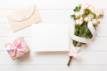 Greeting holiday card mockup with fresh roses on colored table background, mock up with copy space for design.の写真素材