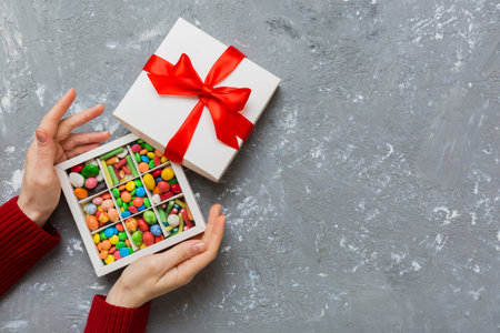 Female hands with delicious candies in box on color background.