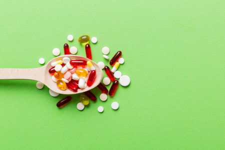 Vitamin capsules in a spoon on a colored background. Pills served as a healthy meal. Red soft gel vitamin supplement capsules on spoon.の写真素材