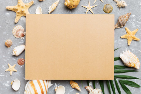 Summer time concept with blank greeting card and blank craft paper on colored background. Seashells from ocean shore in the shape of frame separated with space for text top view.の写真素材