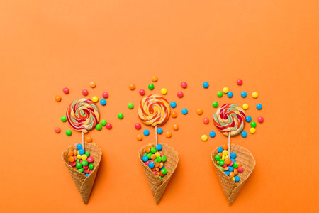 waffle cone full of assorted traditional candies falling out on colored background with copy space....