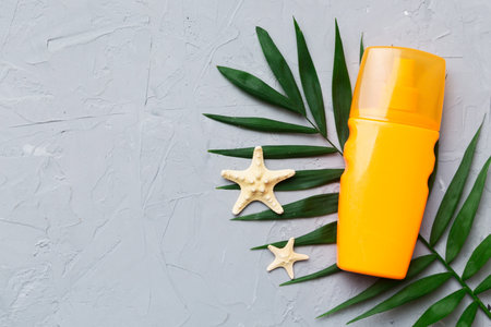 Sunscreen spray bottle. Bottle with sun protection cream and sea shells with tropical green leaf on color background, top view.の写真素材