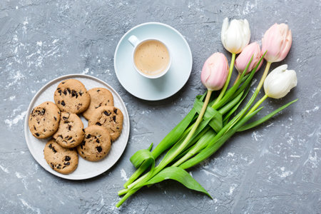 Cup of coffee mug with coffee, cookies and tulips on a colored background. Greeting spring card top view.の写真素材