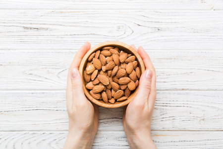 Woman hands holding a wooden bowl with almond nuts. Healthy food and snack. Vegetarian snacks of various nuts.の写真素材