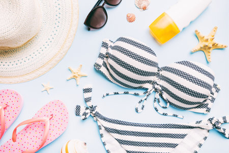 Woman swimwear and beach accessories flat lay top view on colored background Summer travel concept. bikini swimsuit, straw hat and seasheels. Copy space top view.の写真素材