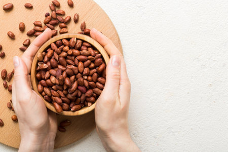 Woman hands holding a wooden bowl with peanuts. Healthy food and snack. Vegetarian snacks of various...