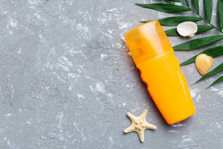 Sunscreen spray bottle. Bottle with sun protection cream and sea shells with tropical green leaf on...