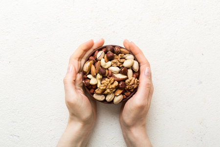 Woman hands holding a wooden bowl with mixed nuts Walnut, pistachios, almonds, hazelnuts and cashews. Healthy food and snack. Vegetarian snacks of various nuts.の写真素材
