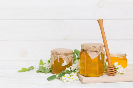 Sweet honey jar surrounded by spring acacia blossoms. Honey flows from a spoon in a jar. jars of clear fresh acacia honey on wooden background.の写真素材